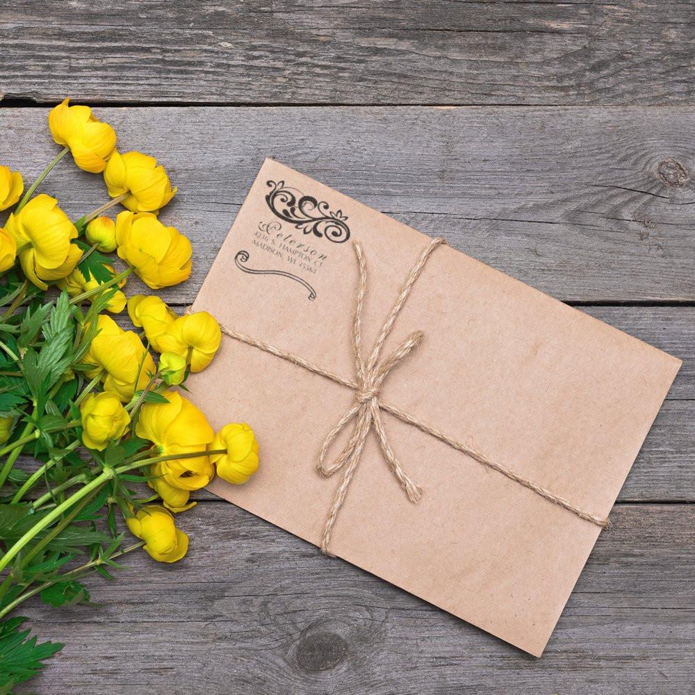 Custom return address rubber stamp on a kraft envelope tied with twine, styled with yellow flowers on rustic wood.