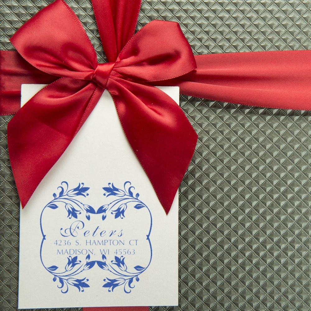 Custom return address rubber stamp with floral frame on gift tag, tied with a red ribbon bow.