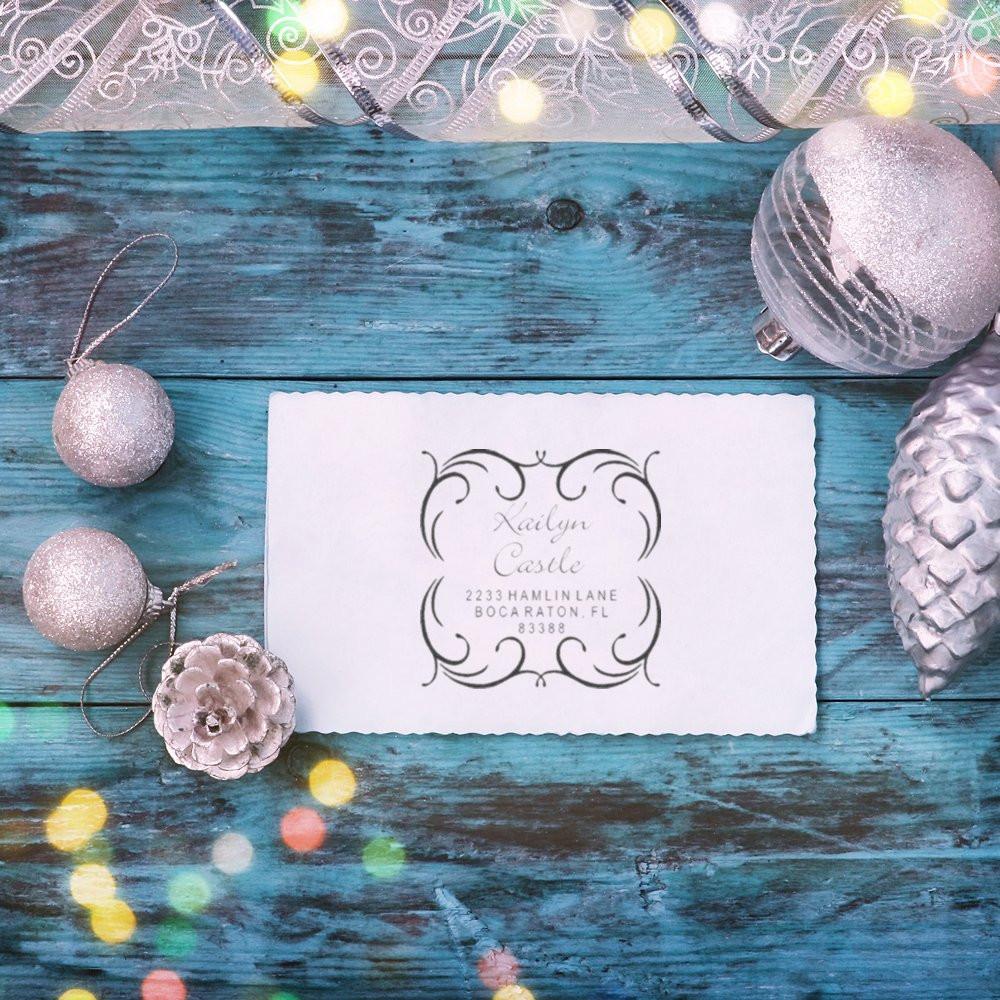 Personalized return address rubber stamp impression on white card, styled with festive silver ornaments and blue wood background.