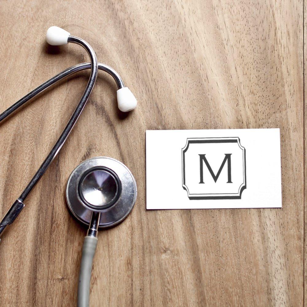 Monogram M rubber stamp design displayed on a card beside a stethoscope on a wood desk.