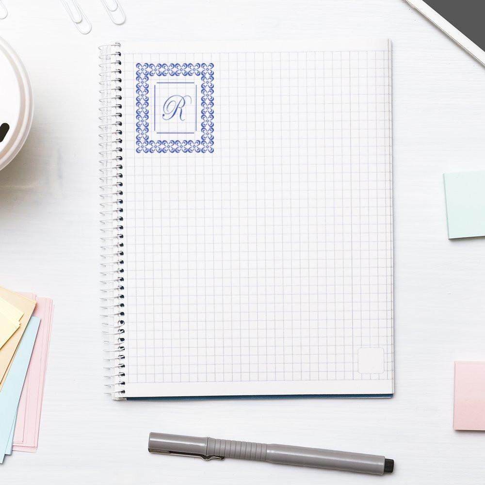 Custom monogram rubber stamp with ornate floral border and letter R stamped on a notebook page for personalized stationery branding.