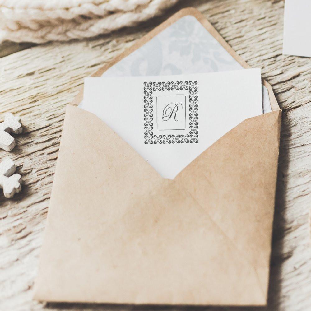 Custom monogram rubber stamp impression on wedding stationery in a kraft envelope.