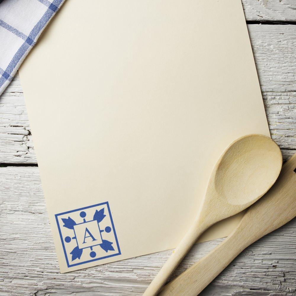 Custom rubber stamp impression on cream paper, featuring a blue monogram design for personalized stationery and craft projects.