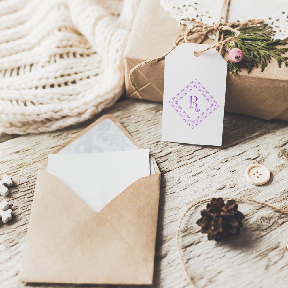 Custom monogram rubber stamp on gift tag and envelope, styled with rustic wrapped presents and twine for elegant packaging.