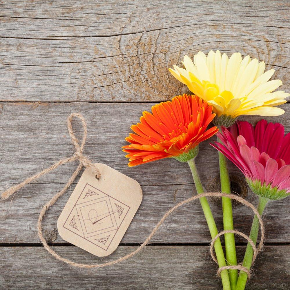 Custom rubber stamp gift tag with floral packaging on rustic wood, tied with twine and accented by colorful gerbera flowers.