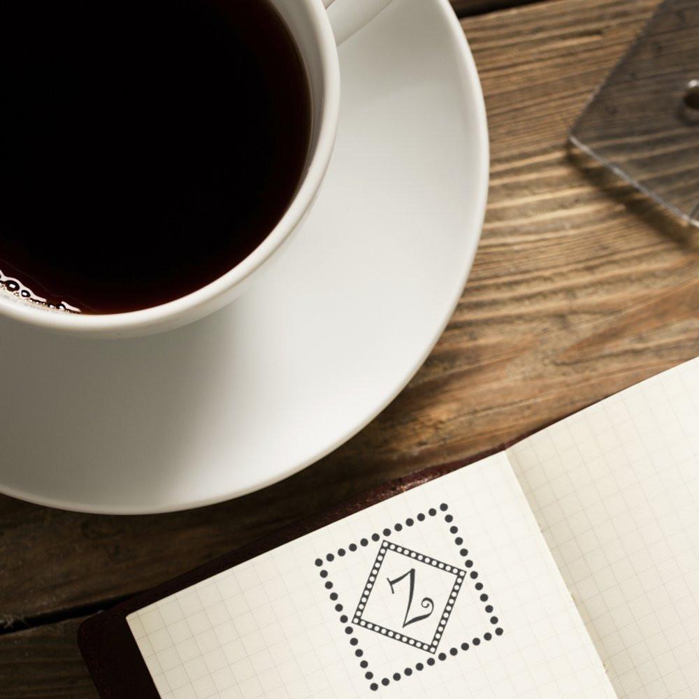 Custom rubber stamp impression in a bullet journal beside coffee on a rustic desk, ideal for planner branding.