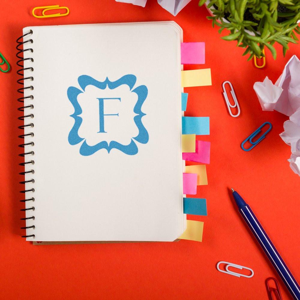Top view of a spiral notebook labeled F for study planning with sticky notes, binder clips, and pen on a bright red workspace.