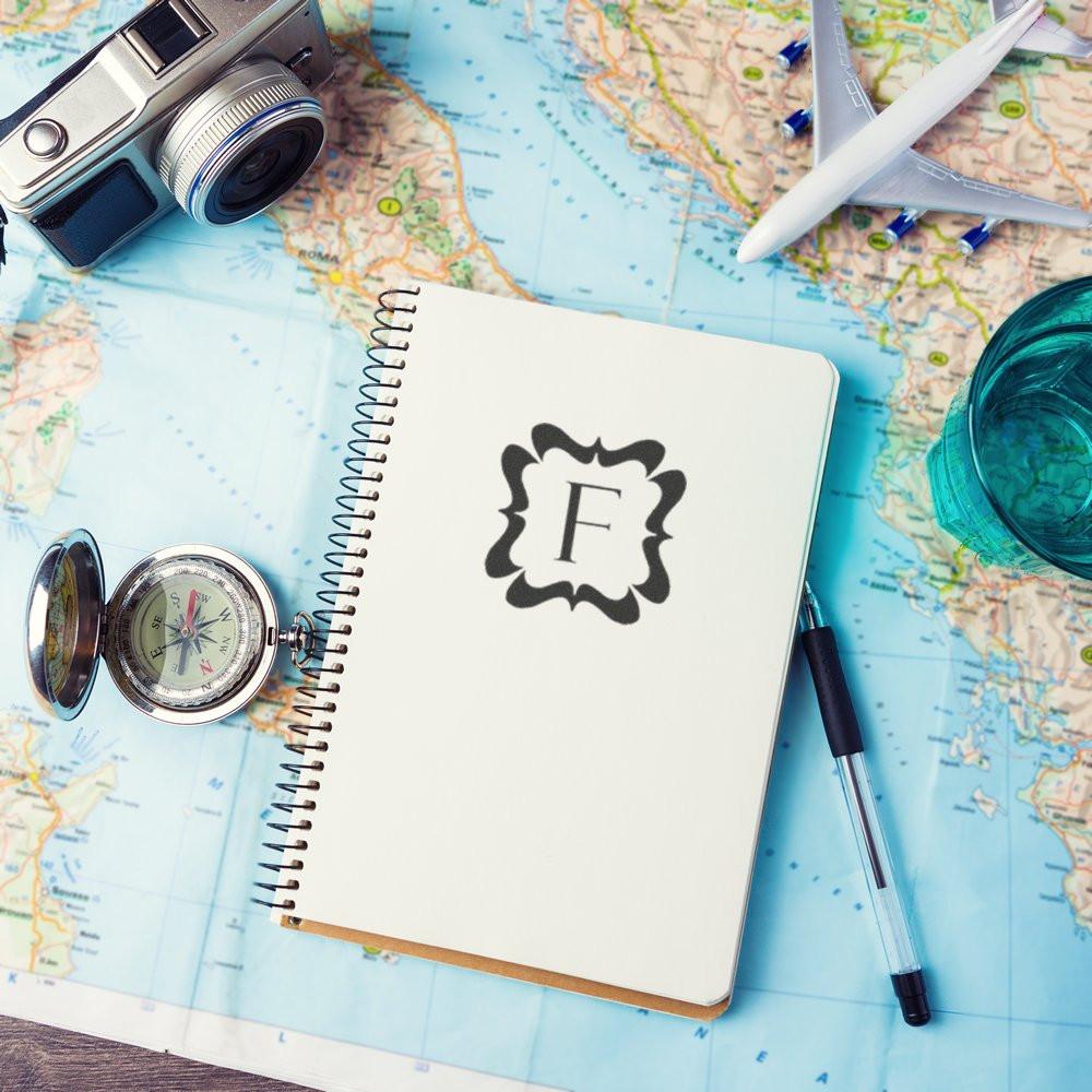 Custom monogram rubber stamp on travel journal notebook with maps, camera, compass and plane for scrapbook branding.