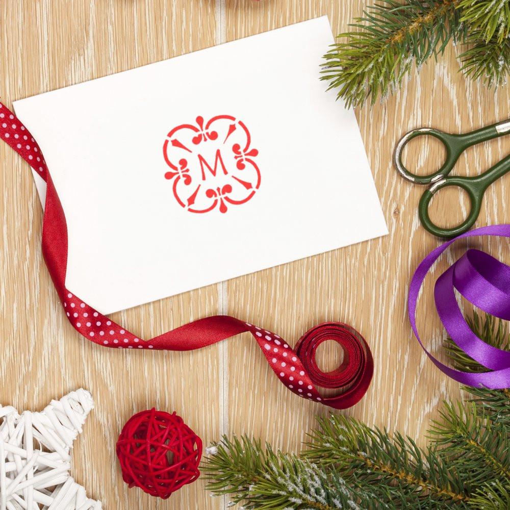 Personalized monogram rubber stamp on a holiday card, styled with ribbon, scissors, and pine for festive DIY gift wrapping.