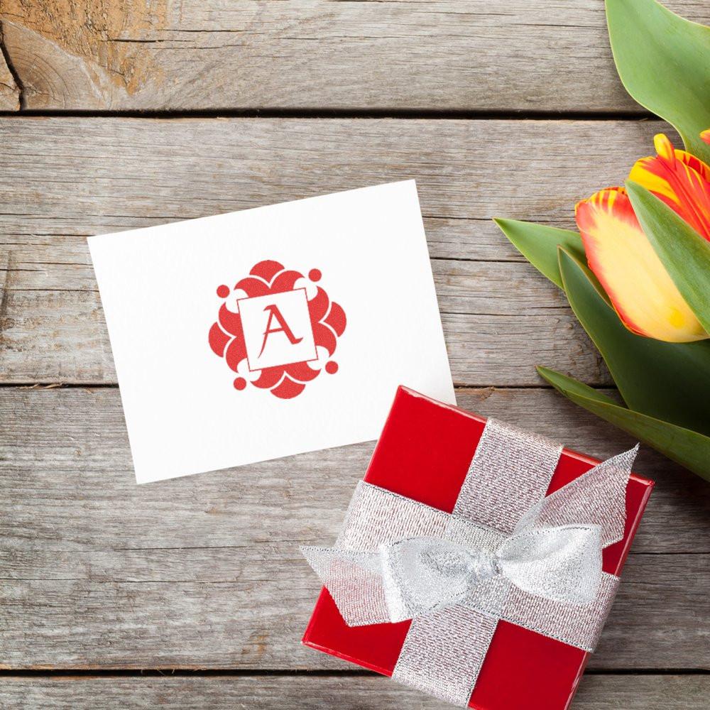 White greeting card with red letter A logo and wrapped gift box with silver ribbon beside tulips on rustic wooden background