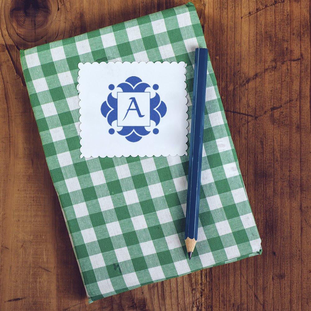 Green checkered notebook with pencil on wooden table, featuring a blue decorative monogram letter A label for personal notes