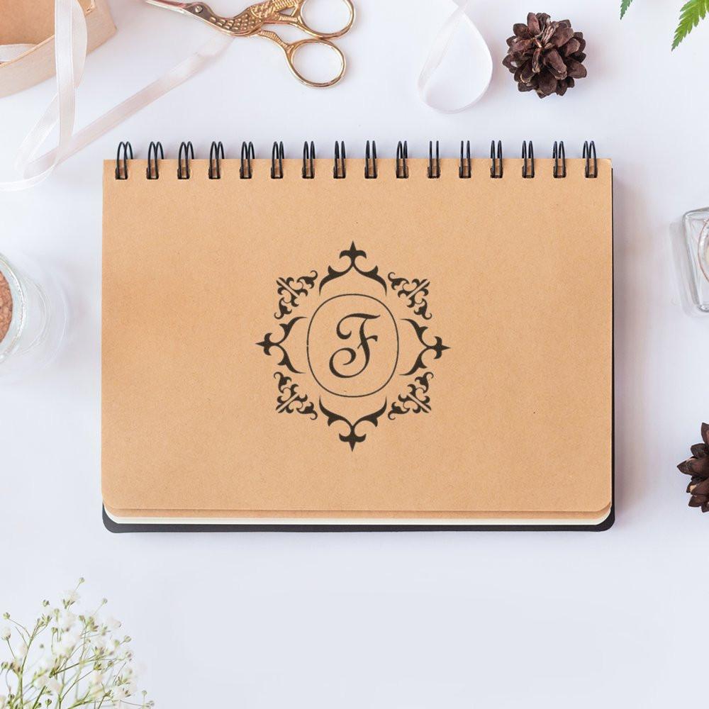Ornate custom monogram rubber stamp with letter F on kraft notebook cover for personalized stationery and crafts.