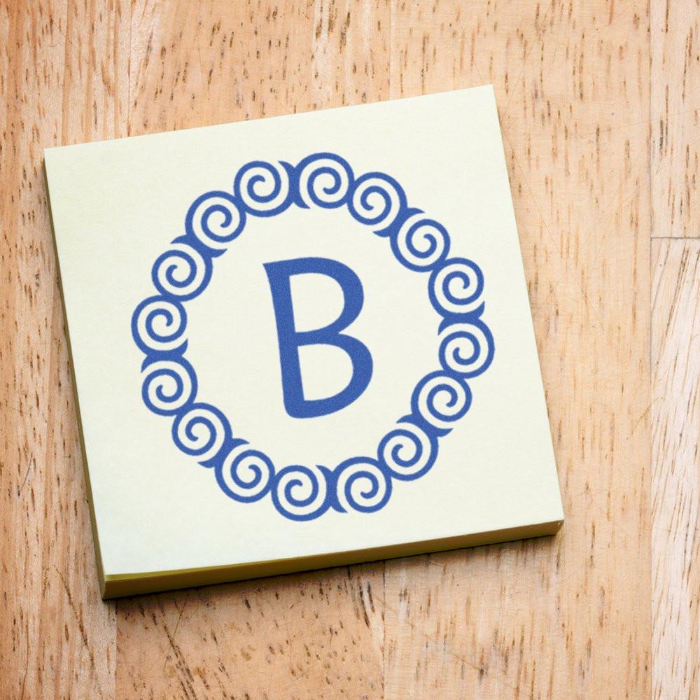 Custom monogram rubber stamp featuring blue letter B in a decorative swirl border on a wooden surface.
