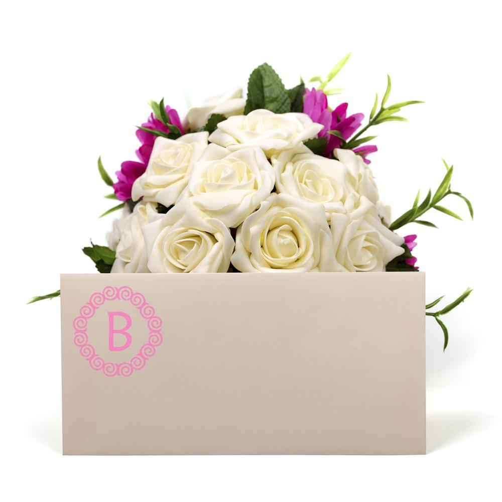 Pink monogram rubber stamp on floral gift bag with white roses, ideal for personalized wedding favors and packaging.
