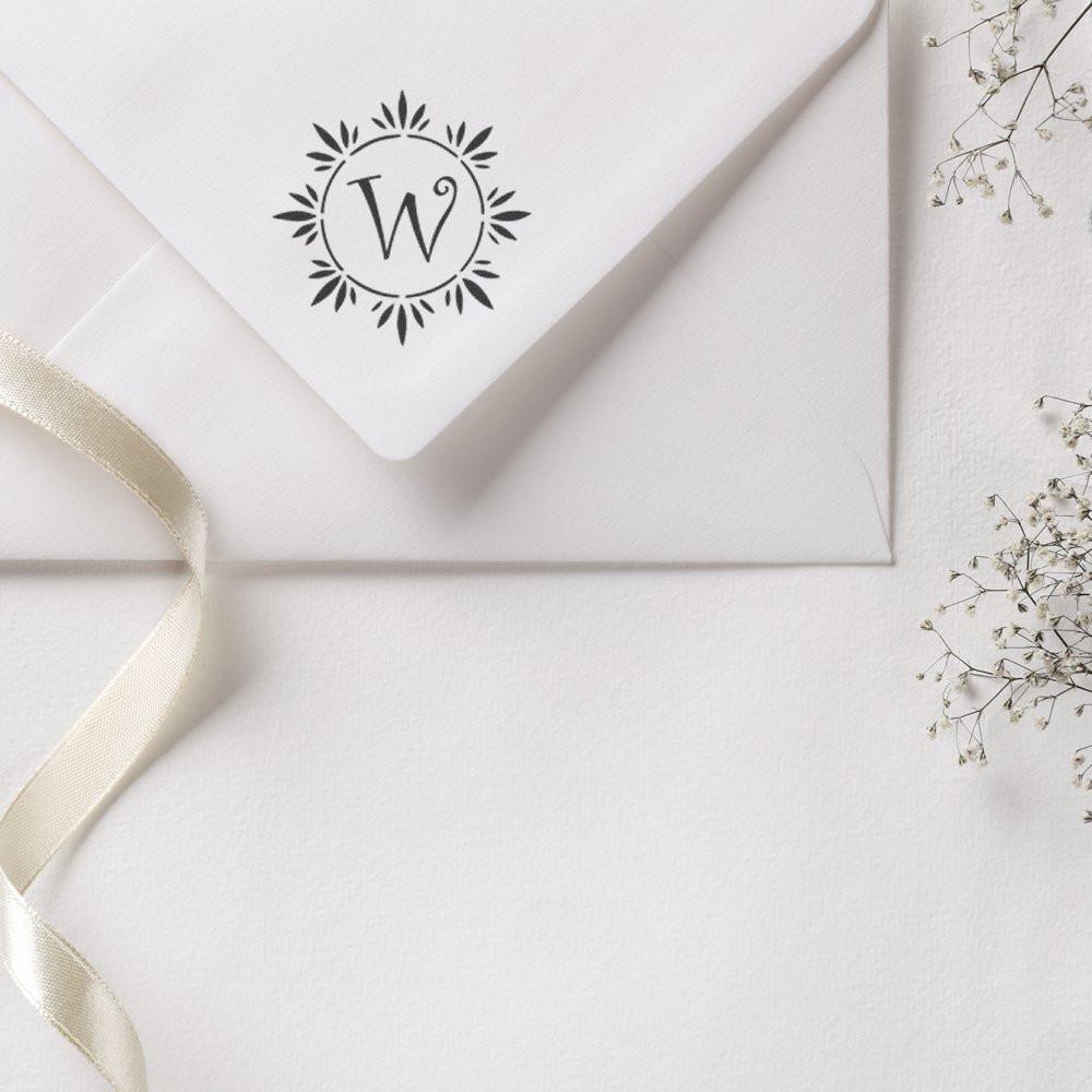 Custom monogram rubber stamp with floral wreath on a white wedding invitation envelope for elegant stationery.