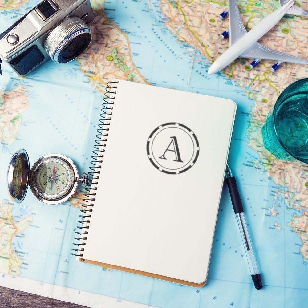 Custom rubber stamp monogram A on a travel journal over a map, ideal for personalized vacation planning and scrapbooks.