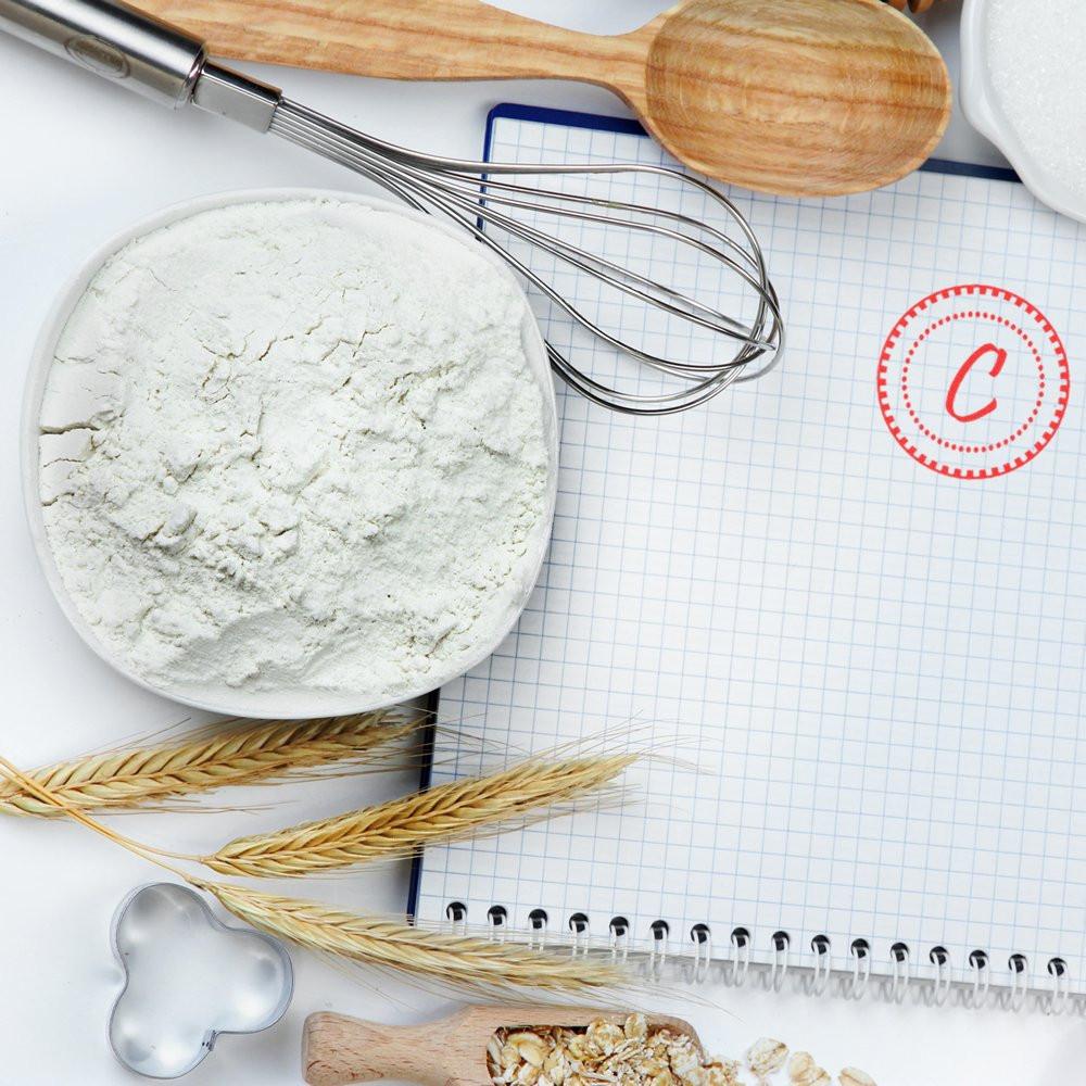 Custom rubber stamp impression on a baking notebook with flour, whisk, wheat, and spoon for bakery branding.