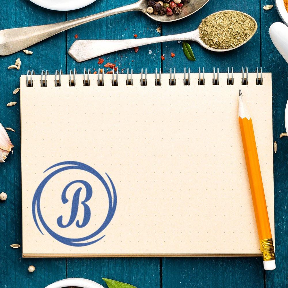 Custom monogram B rubber stamp impression on recipe notebook, ideal for personalized kitchen branding and crafts.