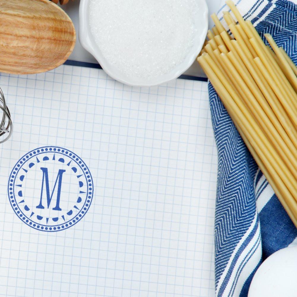 Custom monogram rubber stamp with blue letter M on grid paper, ideal for personalized stationery or kitchen branding.