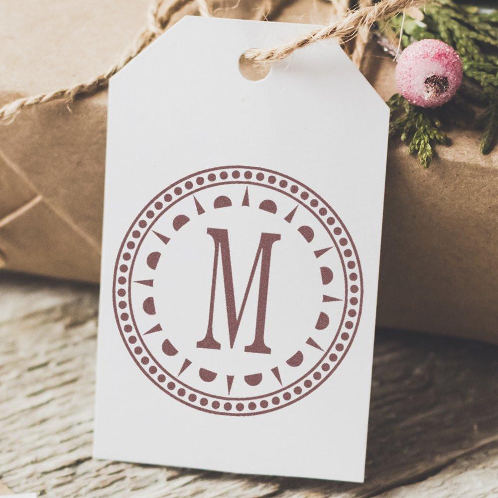 Monogram rubber stamp with letter M on a gift tag for personalized holiday gift wrapping and crafts.