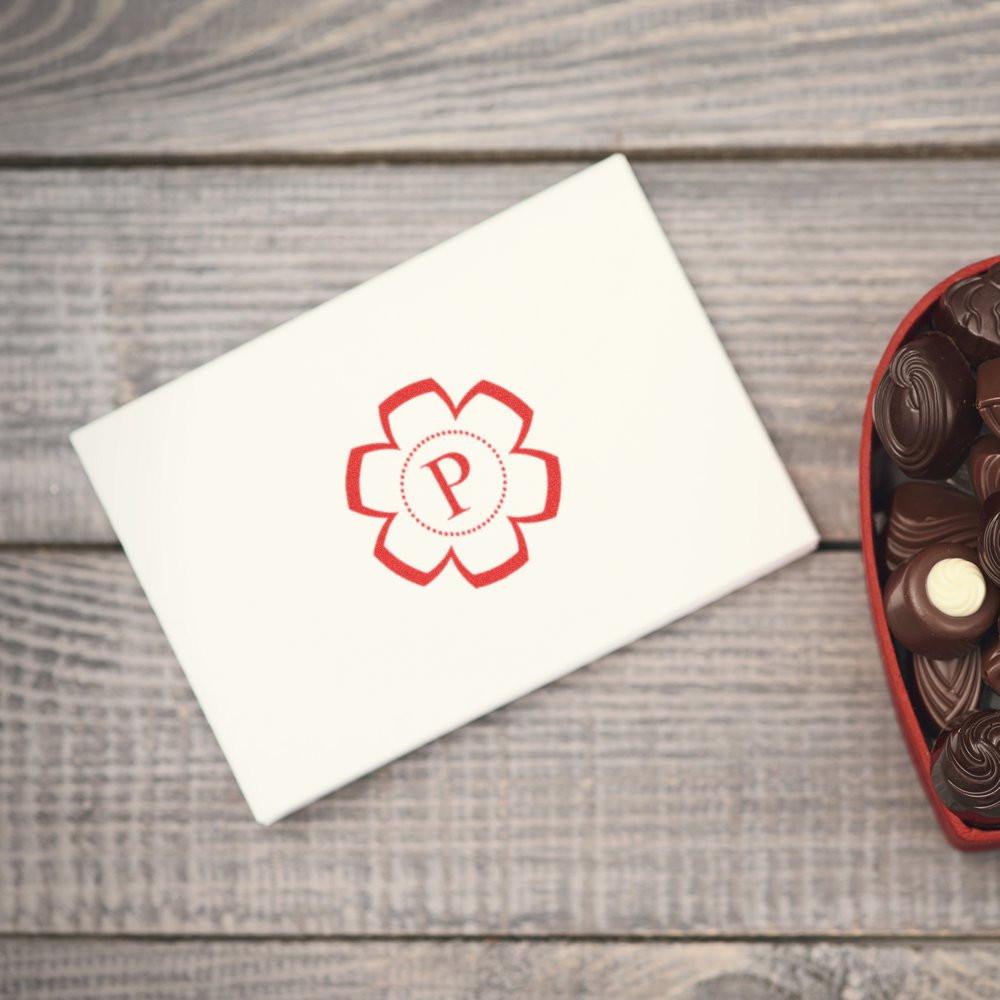 Custom rubber stamp monogram P on white envelope with floral design, next to chocolates on rustic wood table.