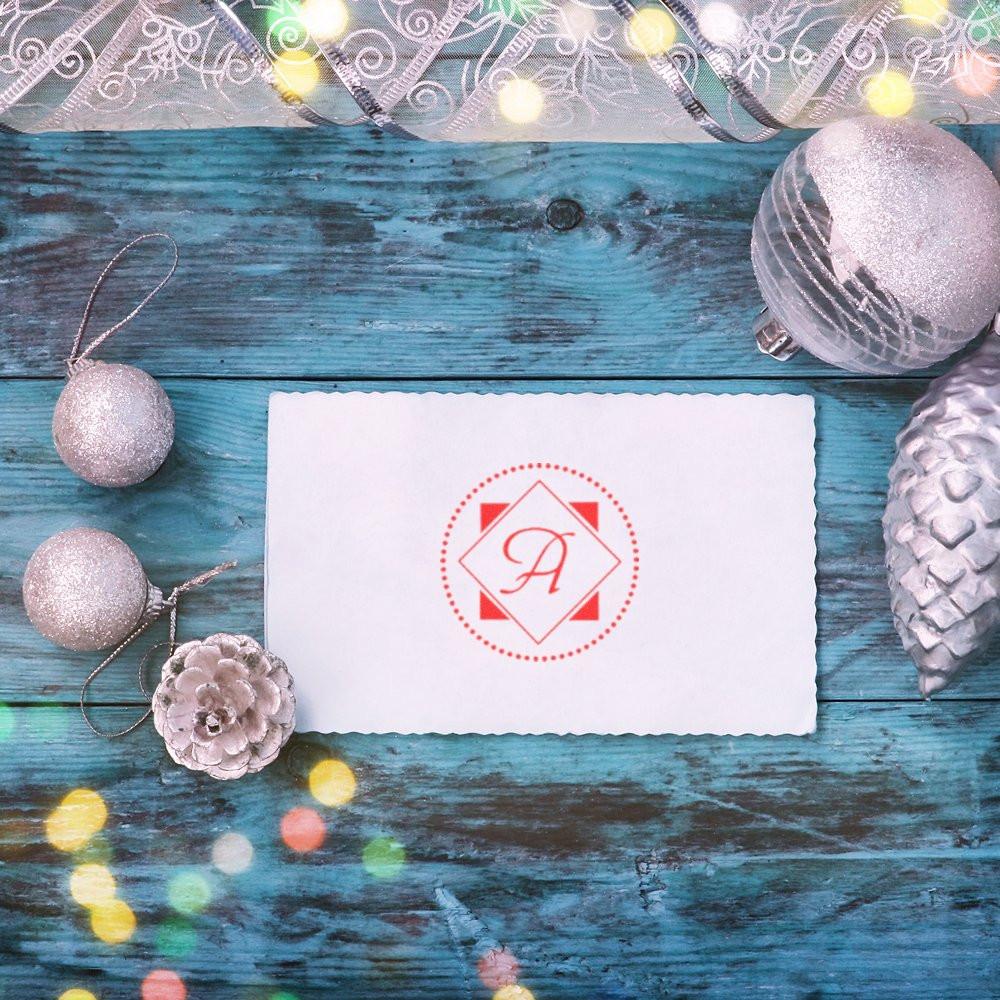 Custom monogram rubber stamp with letter A on a white holiday card, styled with silver ornaments on rustic blue wood.