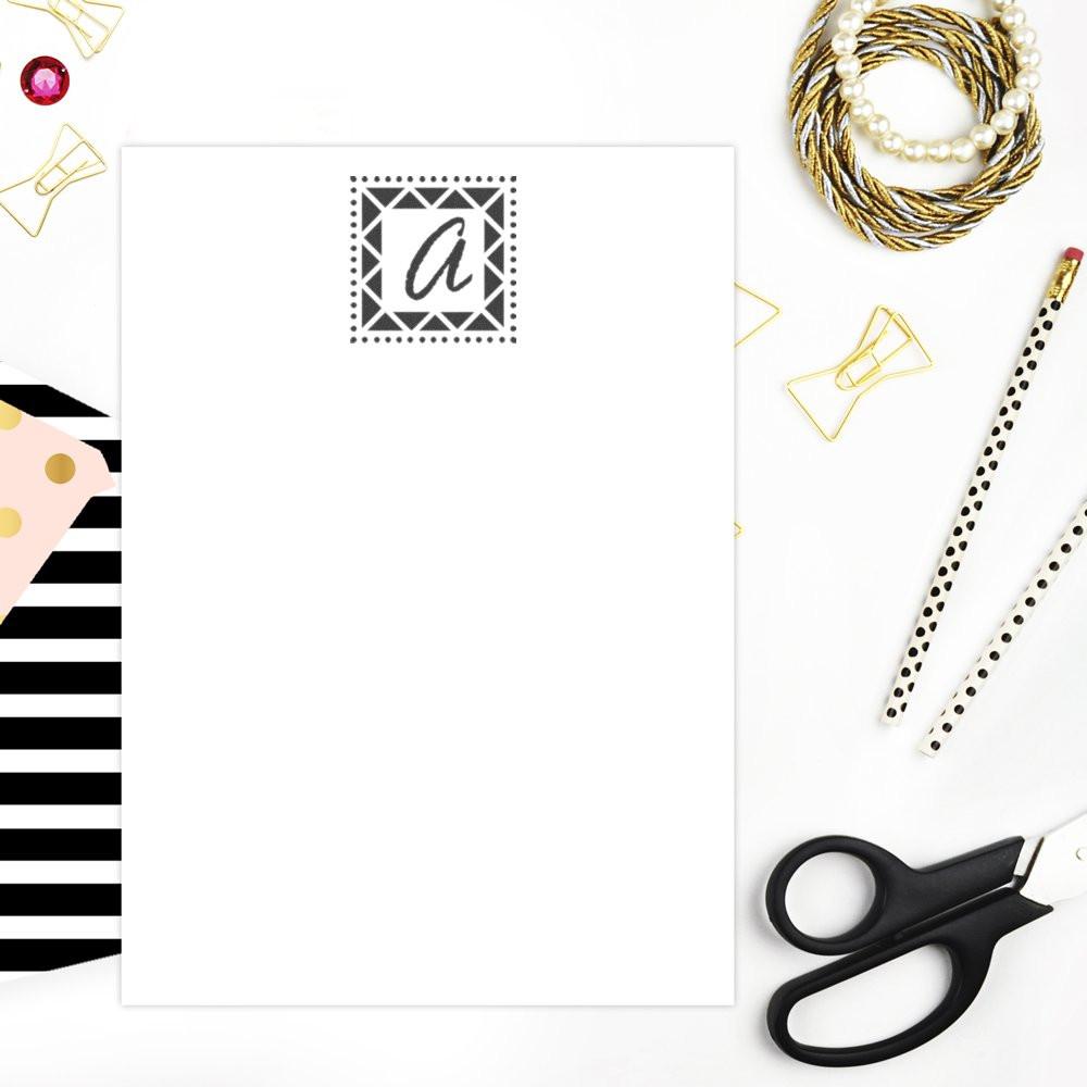 Custom monogram rubber stamp on blank stationery card, styled with paper clips, scissors and craft supplies for branding.