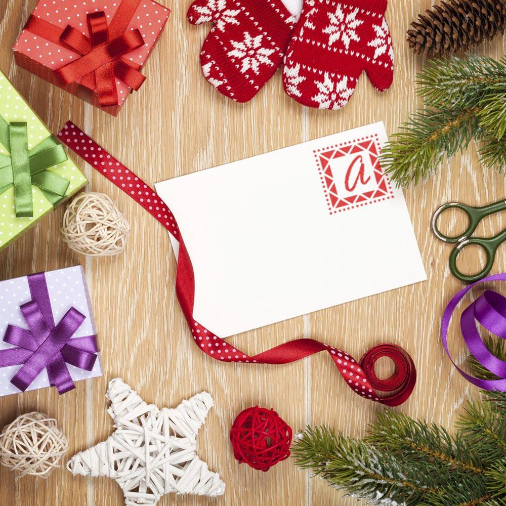 Holiday gift wrapping flat lay with blank card stamped by a custom monogram rubber stamp, plus ribbons, gifts and festive decor.