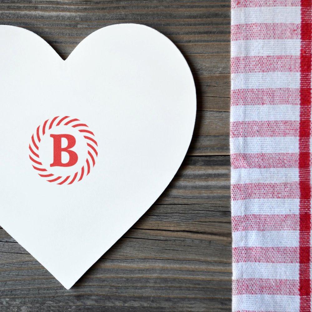 Custom monogram rubber stamp impression with red letter B on a heart-shaped card over rustic wood and gingham fabric.