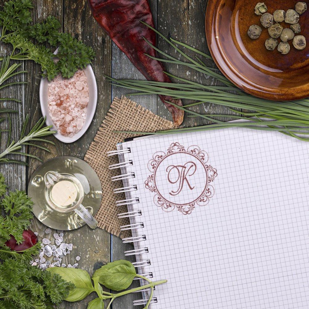 Custom monogram rubber stamp with ornate letter R on notebook, styled with herbs and rustic natural accents.