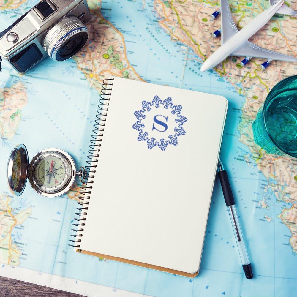 Custom monogram rubber stamp on travel journal with map, camera and airplane for personalized vacation scrapbooking.