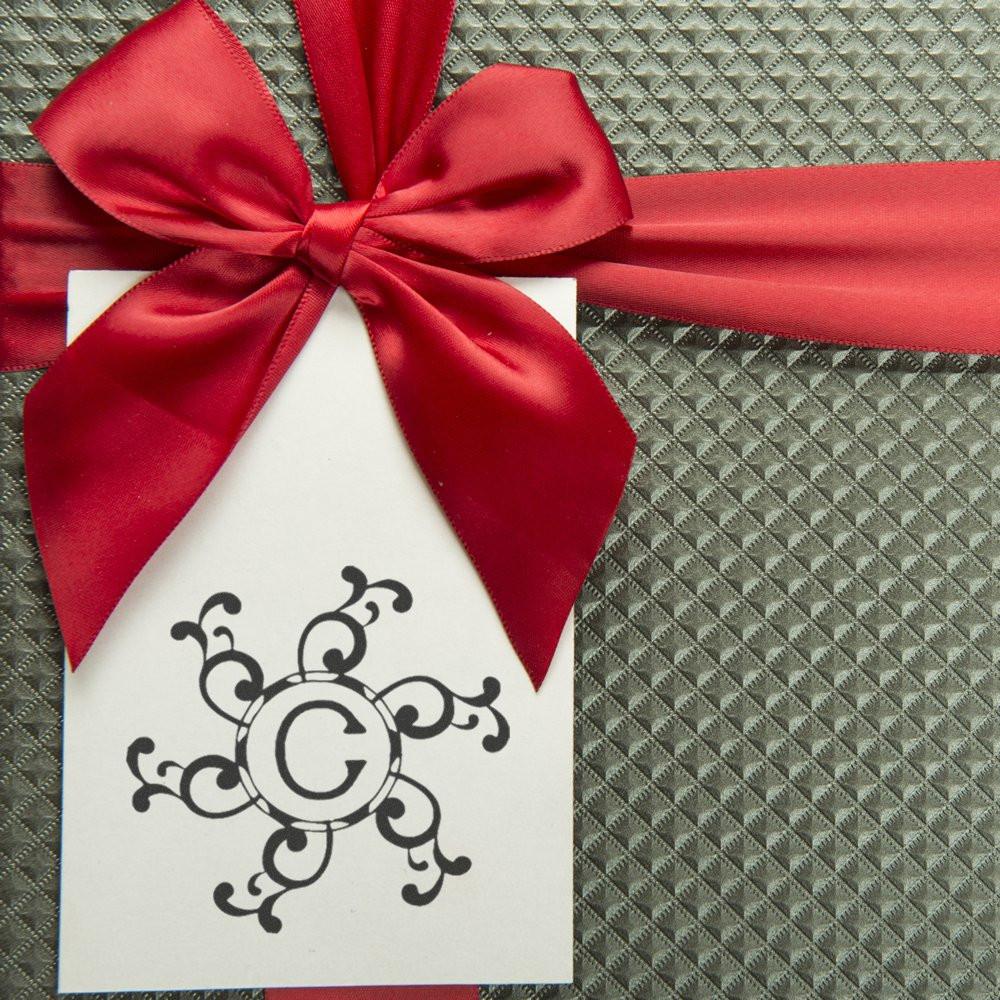 Red satin bow and gift tag with letter C monogram on quilted gray background, decorative holiday present.