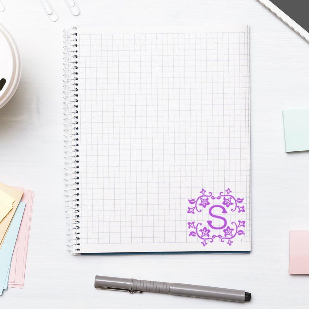 Purple floral monogram S rubber stamp on blank grid notebook, ideal for custom stationery and personalized branding.