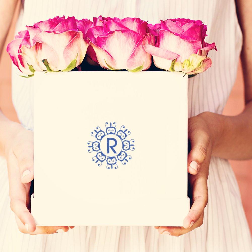 Custom monogram rubber stamp with decorative R on a rose gift box for elegant personalized packaging.