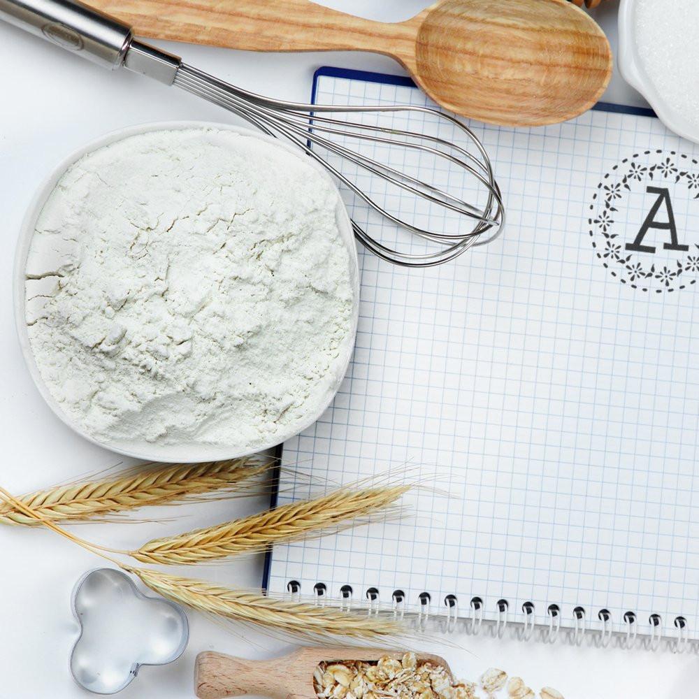 Custom rubber stamp mockup with monogram A on notebook, surrounded by baking tools, flour, and wheat for bakery branding.