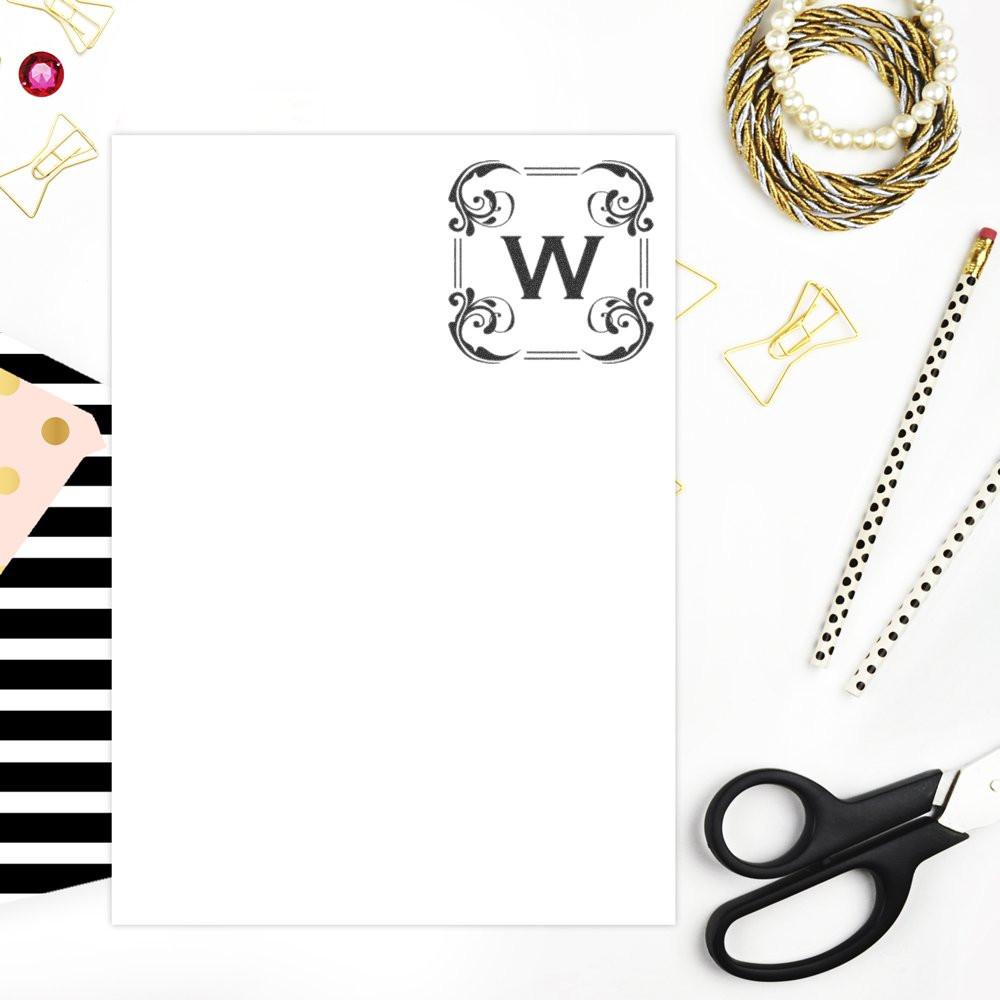 Ornate custom monogram rubber stamp with letter W on blank stationery card, styled with scissors and paper clips.