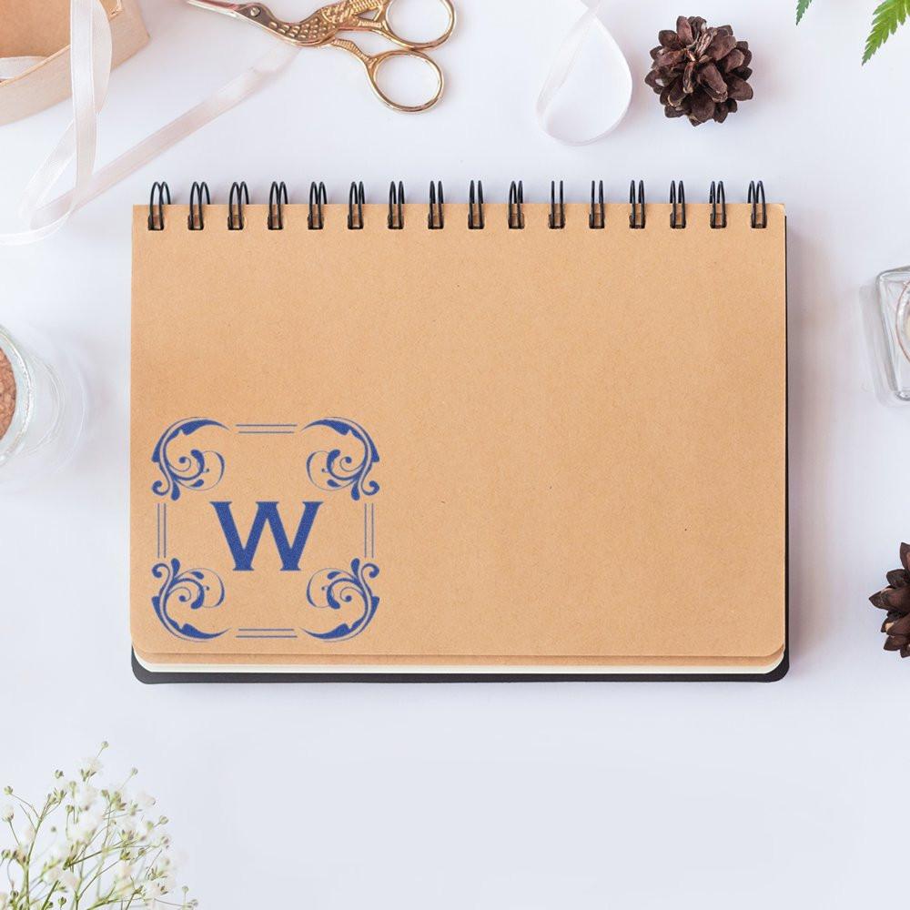 Custom monogram rubber stamp impression with decorative blue letter W on kraft notebook cover for personalized stationery.