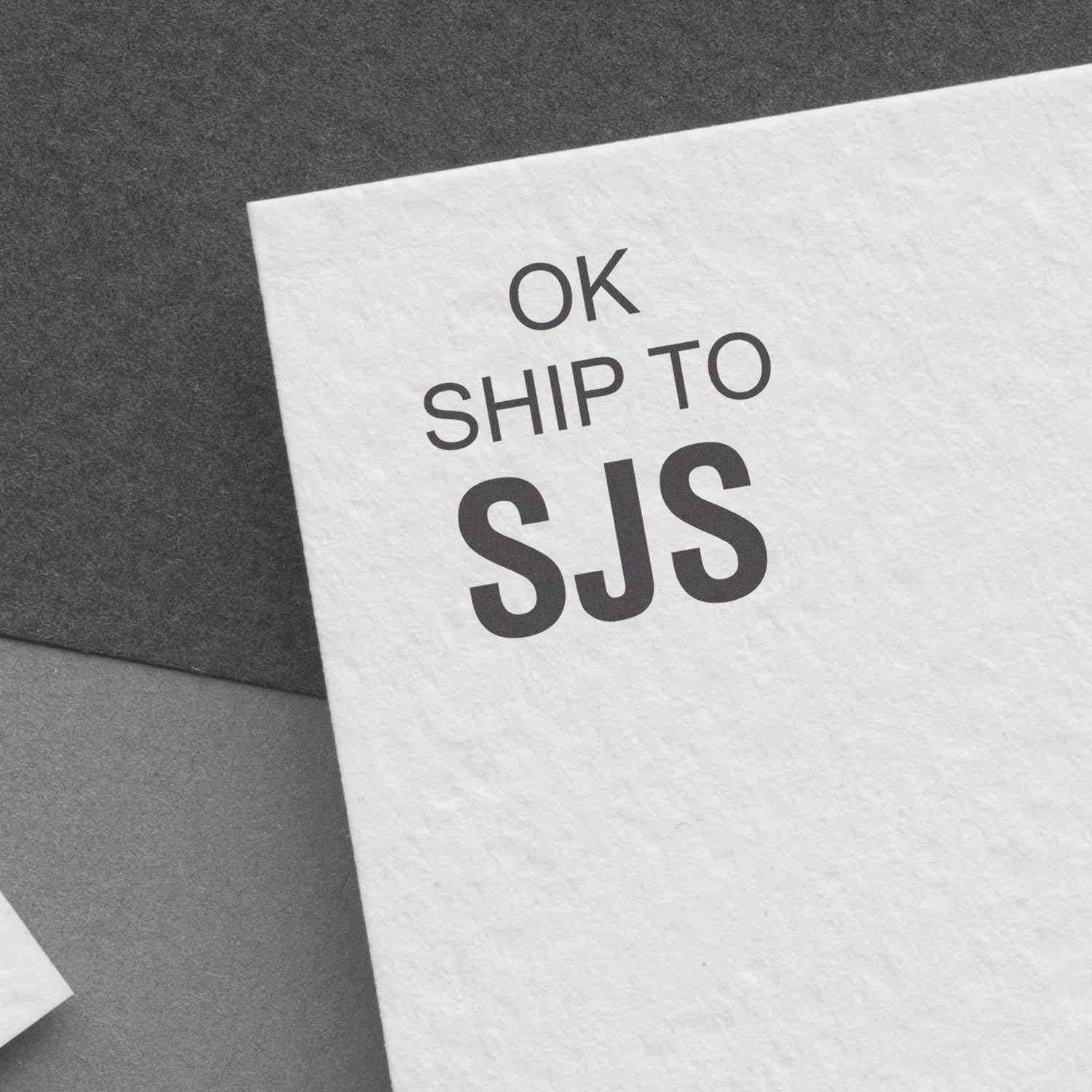 Printed shipping label on white paper reading OK SHIP TO SJS on a dark background.