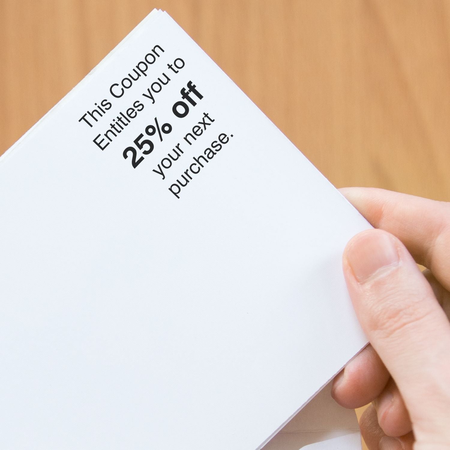 Hand holding a coupon booklet with 25% off your next purchase discount offer printed on white paper.