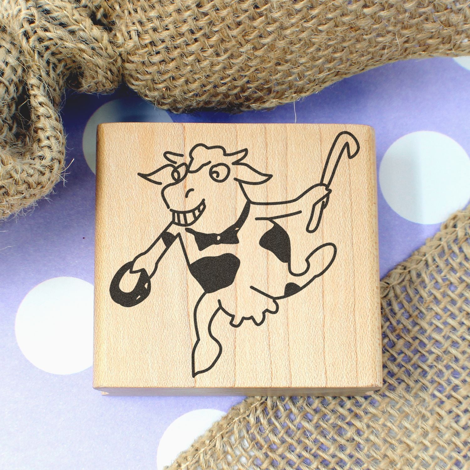 Wooden rubber stamp with smiling dancing cow illustration on burlap and polka dot background