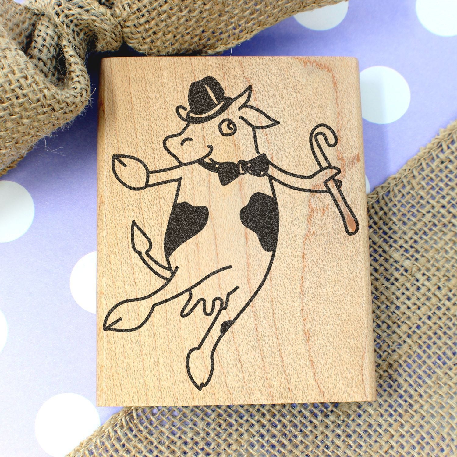 Wooden rubber stamp with a dancing cow illustration wearing a top hat and cane on a polka dot background.