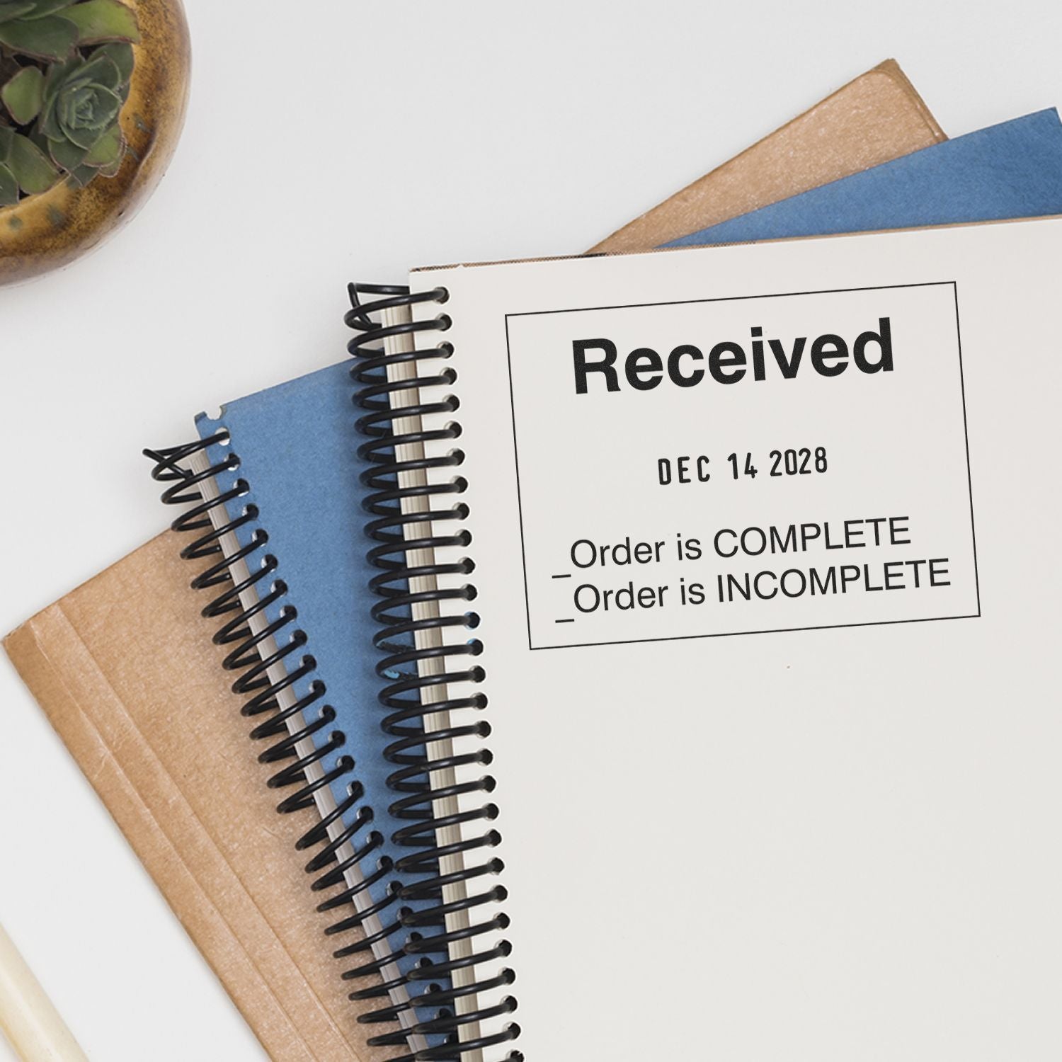 Close-up of spiral notebook and folders with Received stamp for order tracking and document management.