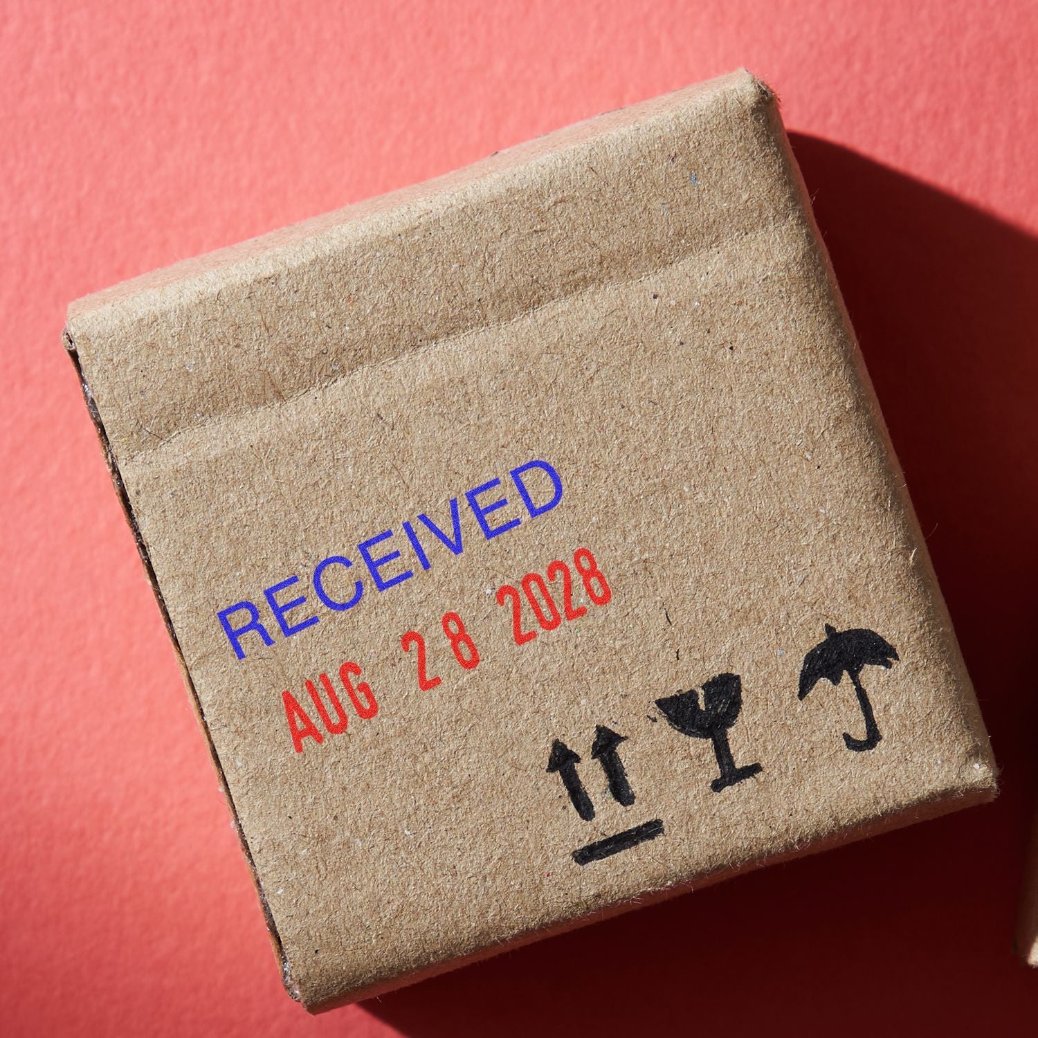 Small cardboard shipping box marked RECEIVED AUG 28 2028 with fragile handling symbols on a red background.