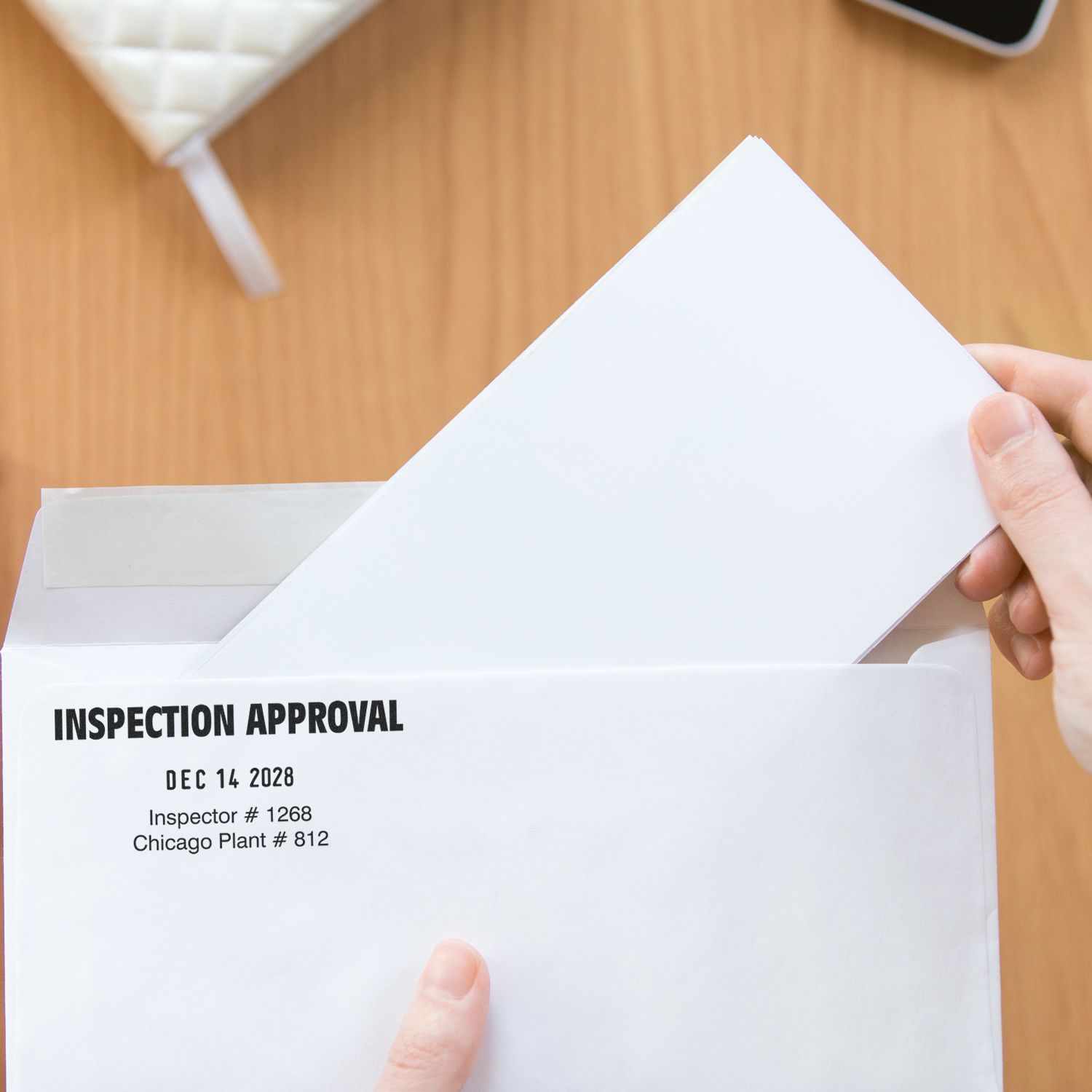 Hand opening an inspection approval envelope with official document on wooden desk, business paperwork concept.