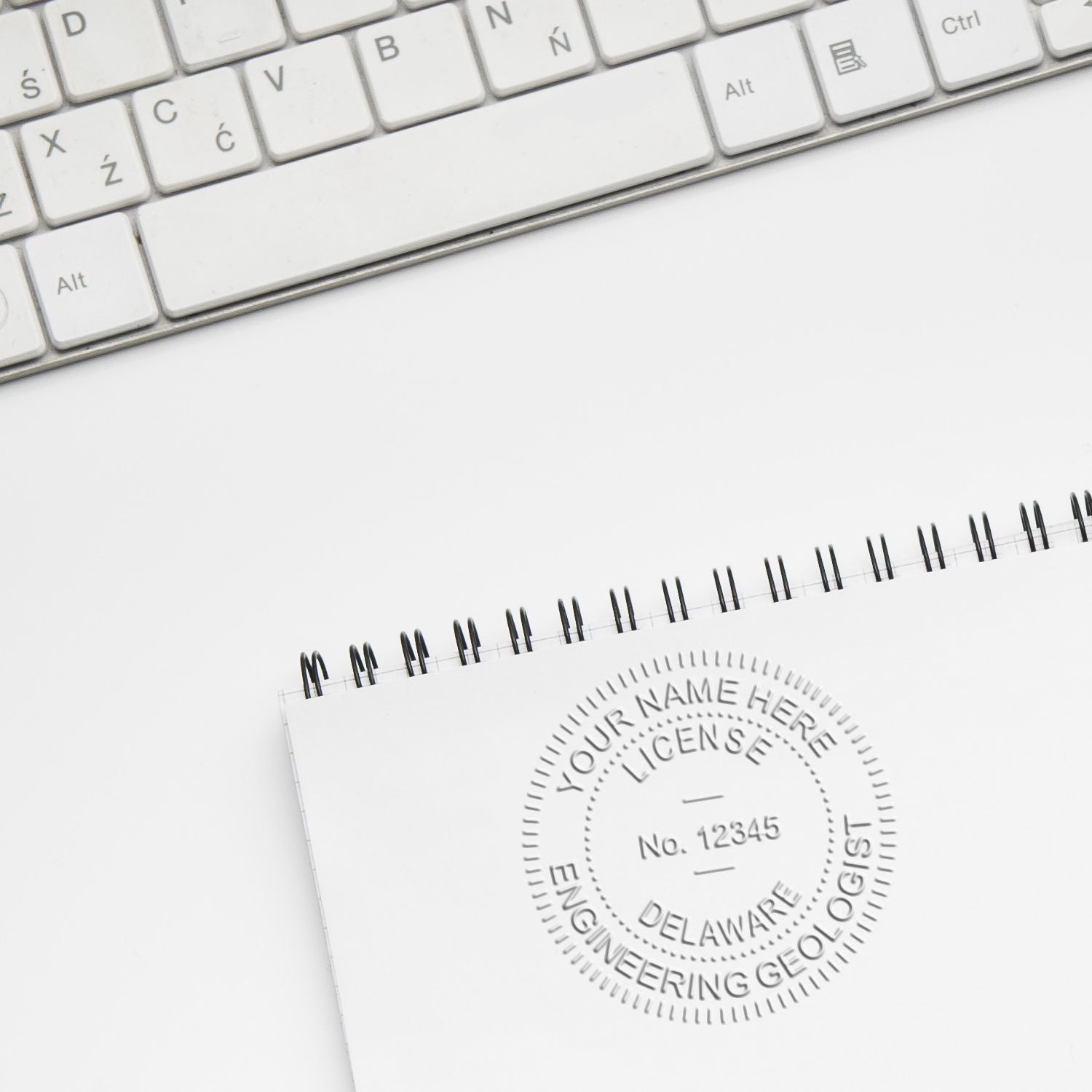 Close-up of white keyboard and spiral notebook with engineering geology license stamp on a clean desk.