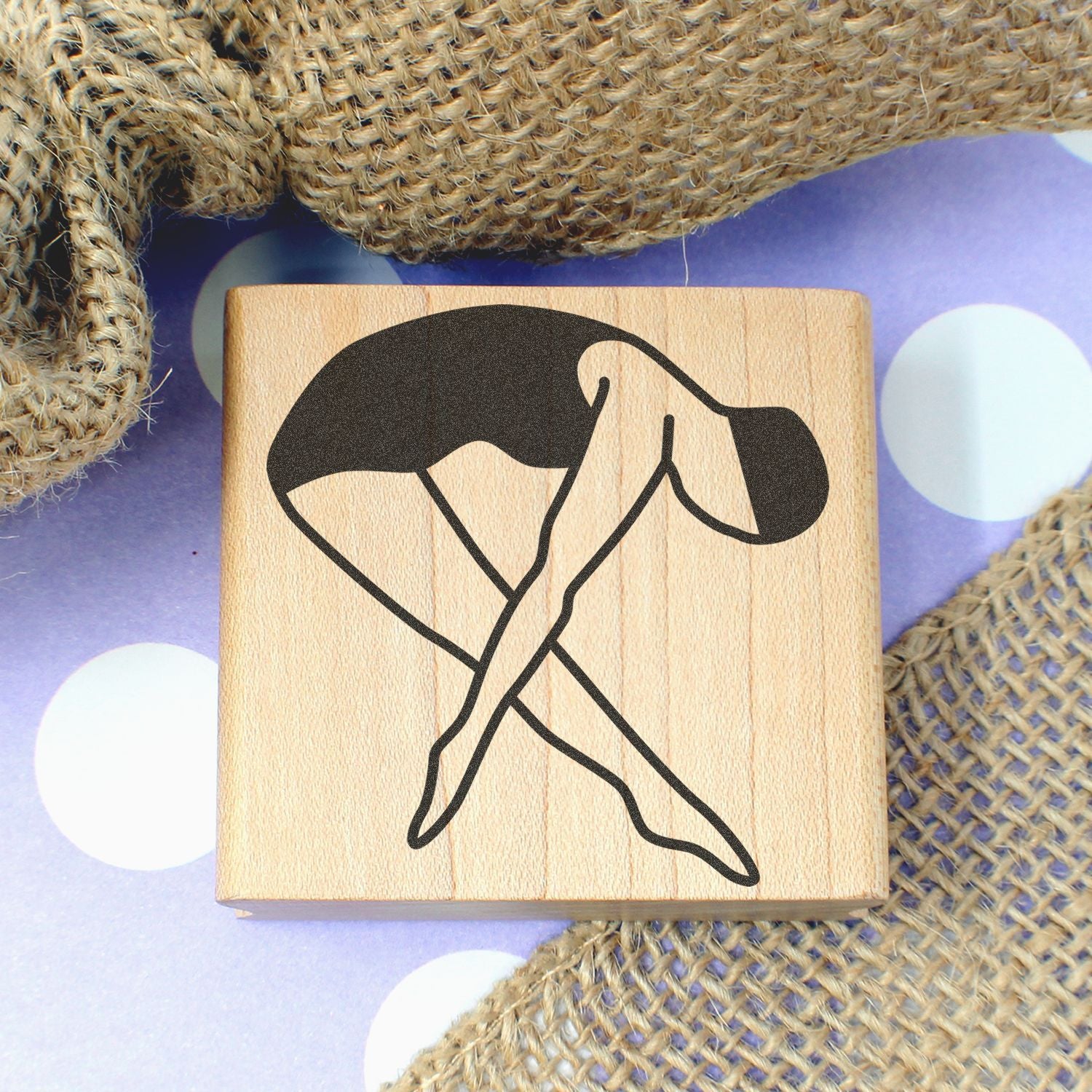 Wooden rubber stamp with black abstract dancer silhouette on a purple polka-dot background and burlap fabric.