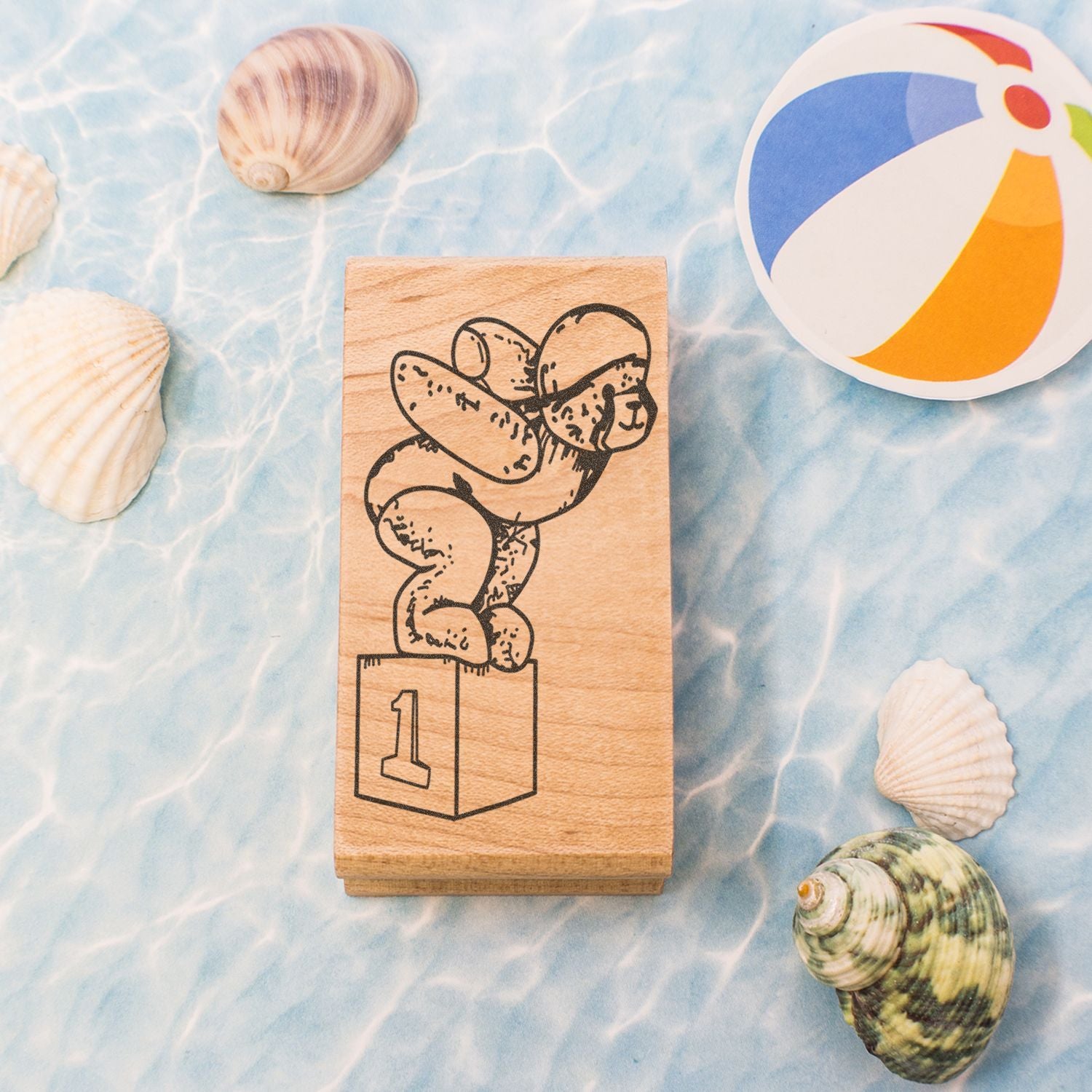 Wooden first-place dog stamp surrounded by seashells and a colorful beach ball on a blue ocean-themed background.