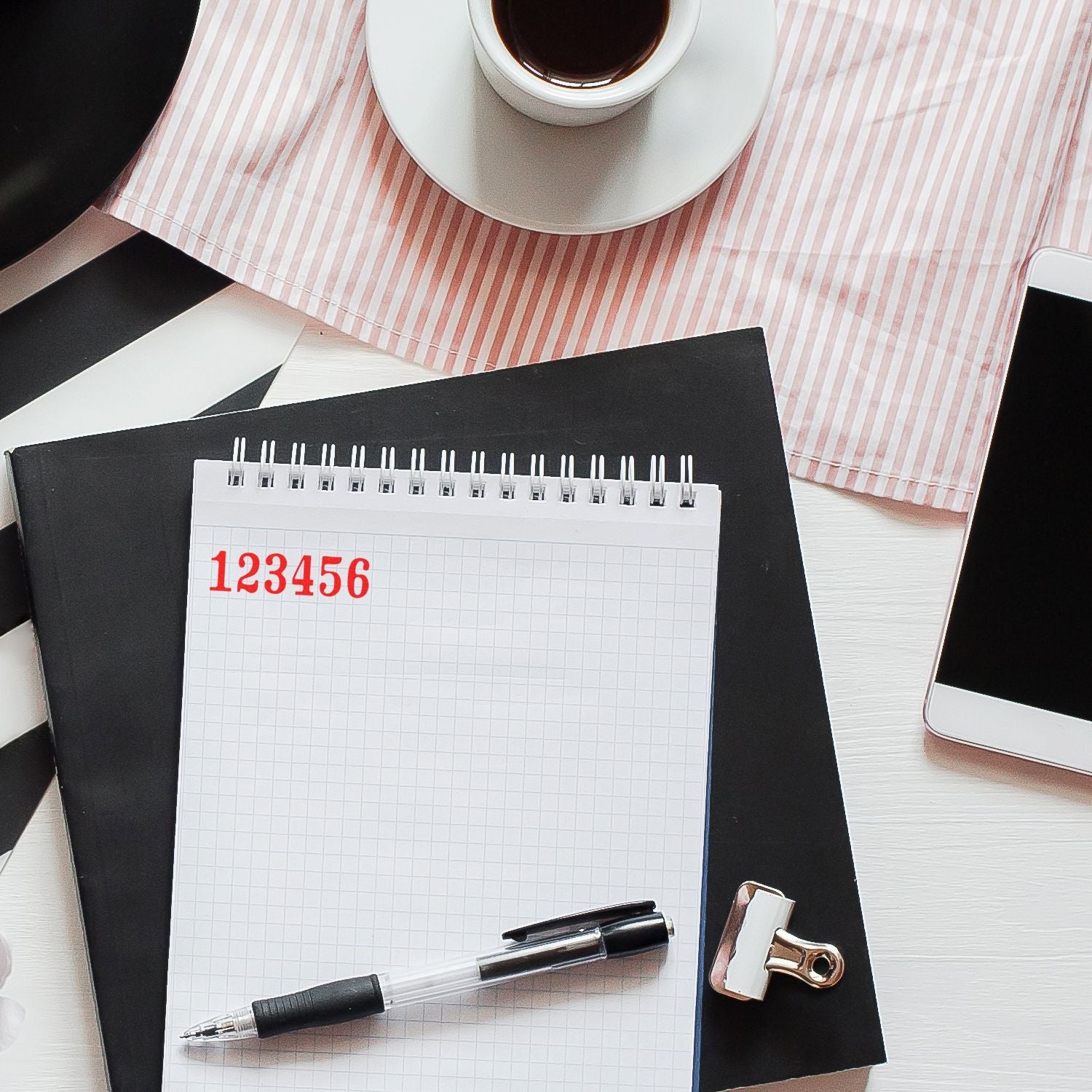 Top view of a stylish office desk with notepad, pen, coffee cup, smartphone, and clipboard in a minimal workspace.