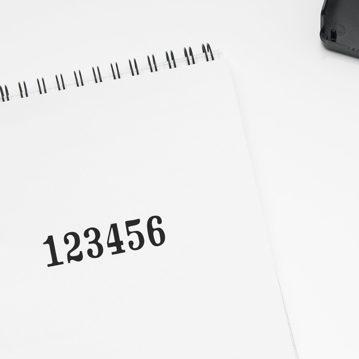 Minimal white spiral notebook with 123456 on cover and calculator on a clean desktop background