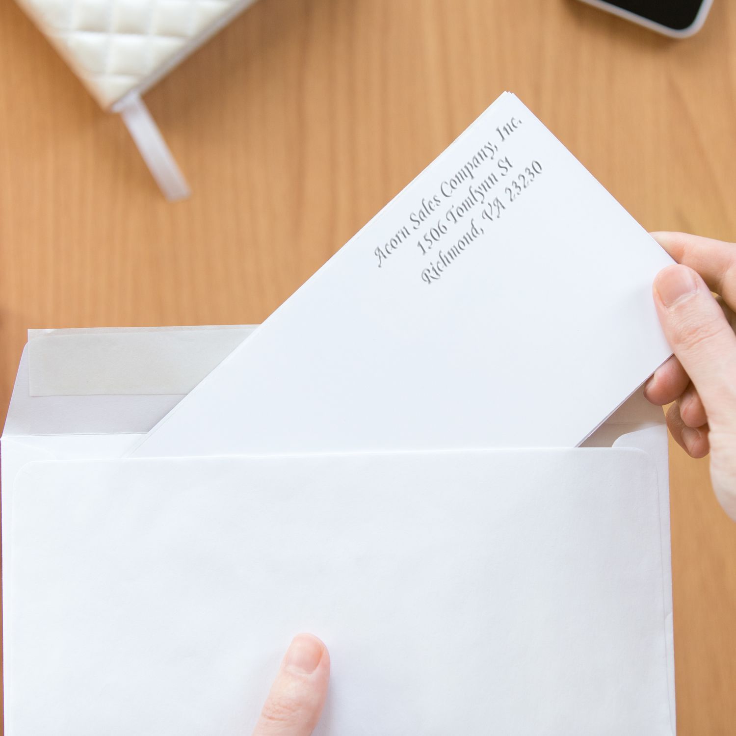 Hand placing a business letter into a white envelope on a wooden desk, close-up office mailing scene.